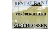 Eine Fensterscheibe mit dem Text 'Vorübergehend geschlossen' in schwarzer Schrift unter dem Wort 'Restaurant'. Draußen ist eine verschwommene Landschaft sichtbar.