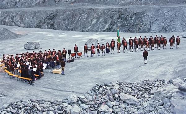 Eine Gruppe von Musikern und Sängern in traditioneller Kleidung versammelt sich in einem Steinbruch für eine Aufführung, mit Instrumenten und Notenpulten.