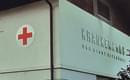 Eingang eines Krankenhauses mit einem roten Kreuz auf einem weißen Schild. Der Schriftzug ist teilweise sichtbar.