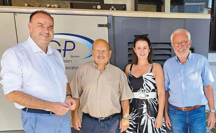 Vier Personen stehen lächelnd vor einem Gebäude mit einem Schild der Firma FGP. Sie sind leger gekleidet, der Hintergrund zeigt technische Ausrüstung.