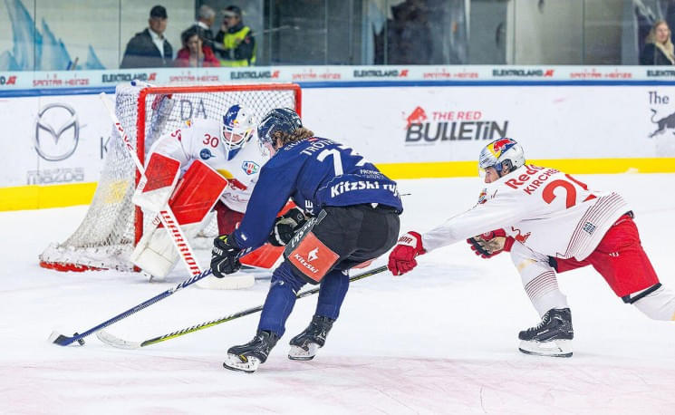 Ein spannendes Eishockeyspiel: Ein Spieler in blauer Ausrüstung greift das Tor an, während ein Spieler in weiß-roter Kleidung versucht, ihn zu stoppen.