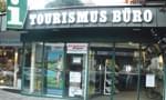 Außenansicht eines Tourismusbüros mit großen Fenstern, Schildern und einem Eingang. Die Aufschrift 'Tourismus Büro' ist deutlich sichtbar.