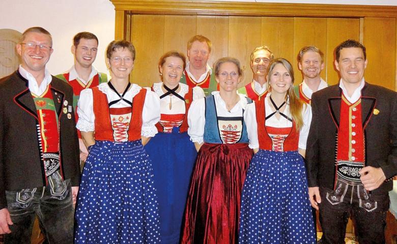 Gruppe von Menschen in traditioneller Tracht, bestehend aus weißen Hemden, roten Westen, gemusterten Röcken und dekorativen Hüten, posiert in einem Raum.