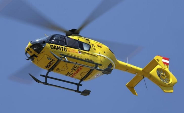 Ein gelber Rettungshubschrauber mit der Aufschrift "ÖAMTC" fliegt am klaren blauen Himmel. Der Hubschrauber trägt österreichische Flaggenmarkierungen.