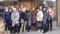 Eine Gruppe von Menschen steht draußen auf einem Bürgersteig vor einem Geschäft und posiert für ein Foto. Sie tragen Winterkleidung und lächeln in die Kamera.