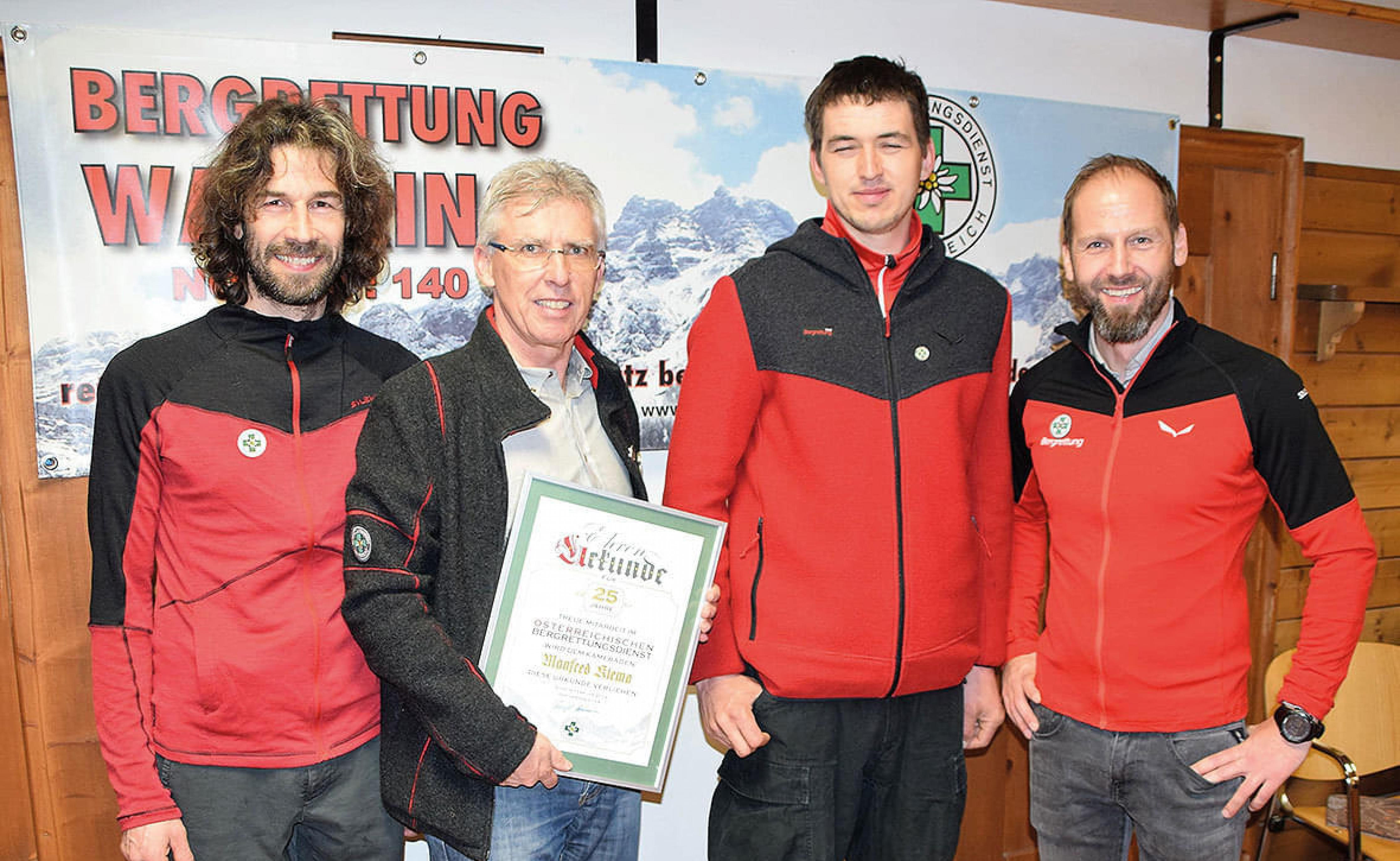 Vier Männer in roten und schwarzen Jacken stehen vor einem Schild. Ein Mann hält eine Urkunde. Sie lächeln in die Kamera.