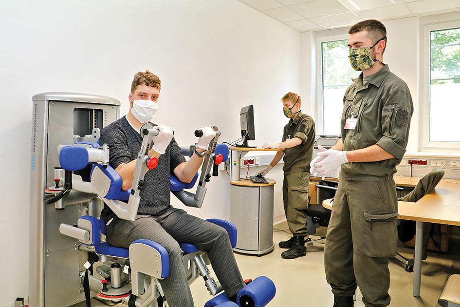 Militärpersonal in einem Labor führt Tests an einem medizinischen Gerät durch, das einer Person hilft, Armbewegungen zu trainieren.