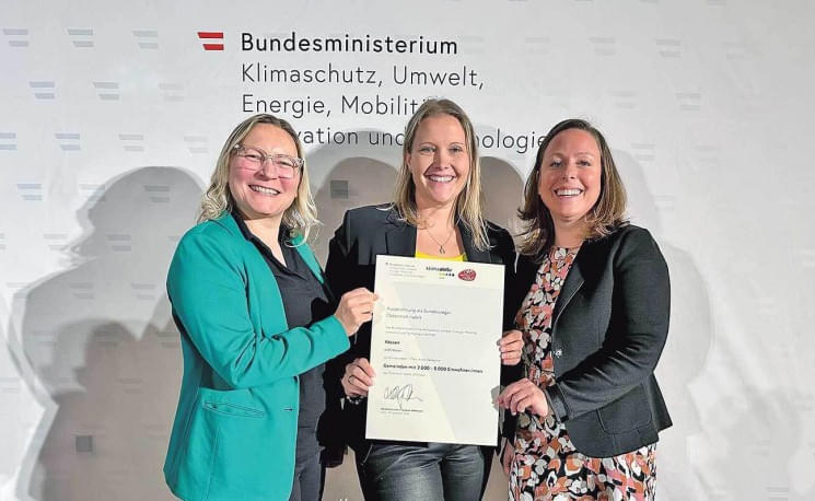 Drei Frauen halten eine Urkunde vor einem Banner des Bundesministeriums für Klimaschutz, Umwelt, Energie, Mobilität, Innovation und Technologie.