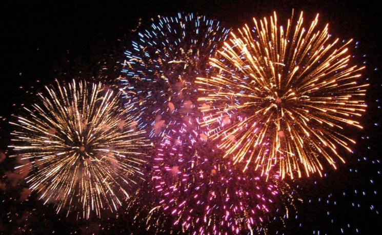 Buntes Feuerwerk am Nachthimmel mit leuchtenden, sternförmigen Explosionen in verschiedenen Farben wie Blau, Lila und Gold vor einem dunklen Hintergrund.