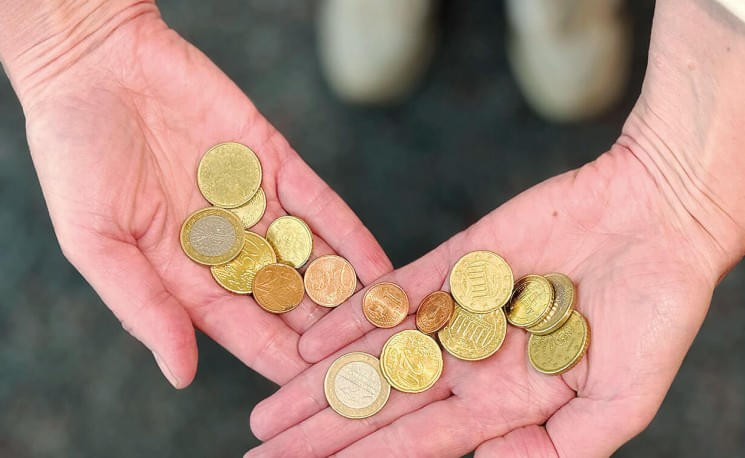 Zwei offene Hände, die verschiedene Euro-Münzen halten, auf einem unscharfen Hintergrund. Die Münzen sind in unterschiedlichen Größen und Farben.