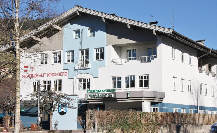 Ein zweistöckiges Gebäude mit hellblauer Fassade. Ein Schild mit der Aufschrift 'Gemeindeamt Kirchberg'. Der Himmel ist klar und blau.