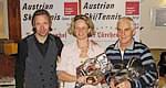 Drei Personen bei einer Preisverleihung, halten Trophäen in den Händen; im Hintergrund Banner mit der Aufschrift 'Austrian SkiTennis'."