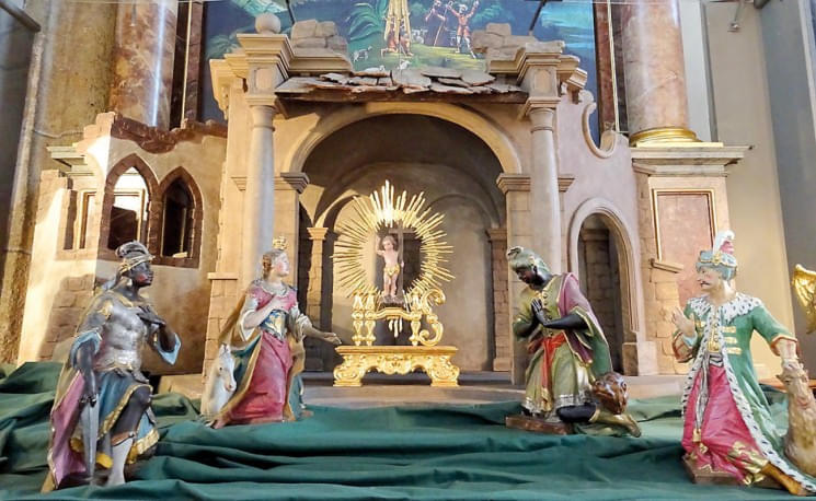 Eine prächtige Krippenszene in einer Kirche, mit kunstvoll bemalten Statuetten der Heiligen Drei Könige vor einem Altar mit strahlender Madonna.