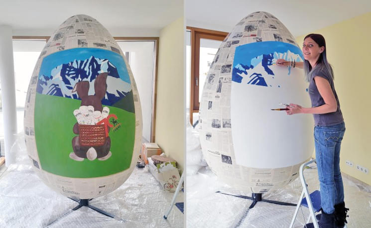 Zwei Bilder zeigen eine Frau, die ein großes Ei bemalt. Links ein Bergpanorama mit Tieren, rechts ist der Hintergrund noch blau und unvollständig.