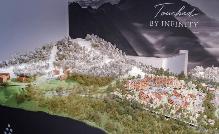 Modell einer hügeligen Landschaft mit Gebäuden, umgeben von Wald, und einem Schriftzug "Touched by Infinity" auf einem dunklen Hintergrund.