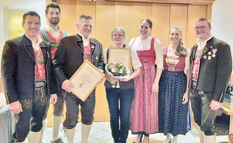 Eine Gruppe von Menschen in traditioneller bayerischer Tracht posiert für ein Foto, zwei Personen halten Urkunden, eine Frau hat einen Blumenstrauß.