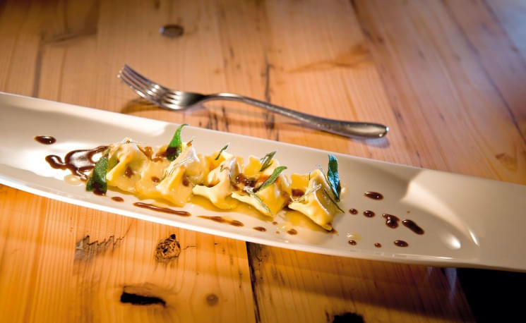Elegante Präsentation von gefüllten Teigtaschen auf einem langen, weißen Teller mit dunkler Soße, garniert mit frischen Kräutern, auf einem Holztisch.