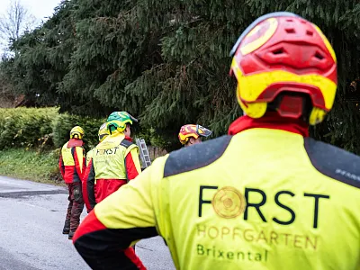 Mehrere Personen in rot-gelber Schutzkleidung stehen an einer Straße im Wald. Auf der Kleidung steht "Forst Hopfgarten Brixental".
