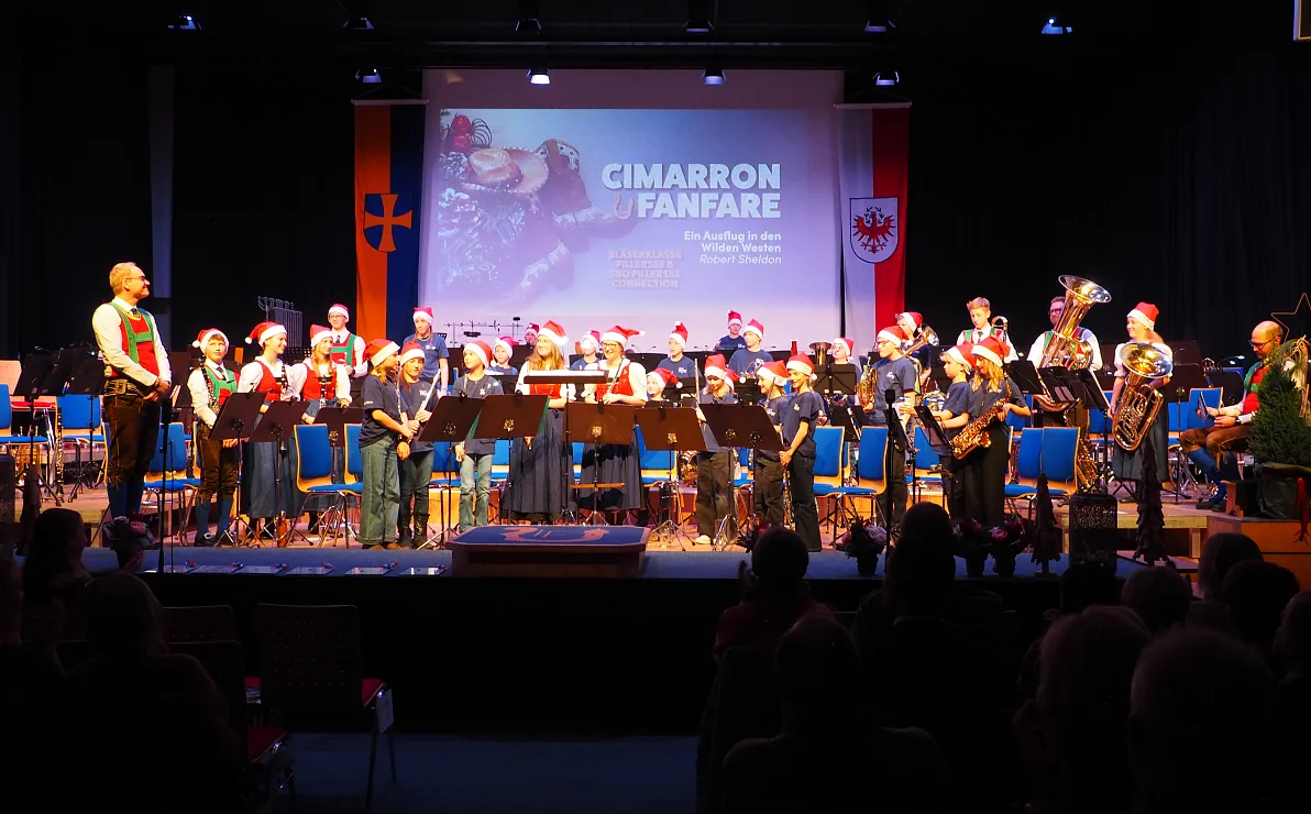 Eine Blaskapelle in traditioneller Tracht spielt auf einer Bühne, beleuchtet von Bühnenlichtern. Im Hintergrund ein Banner mit der Aufschrift "Cimarron Fanfare".