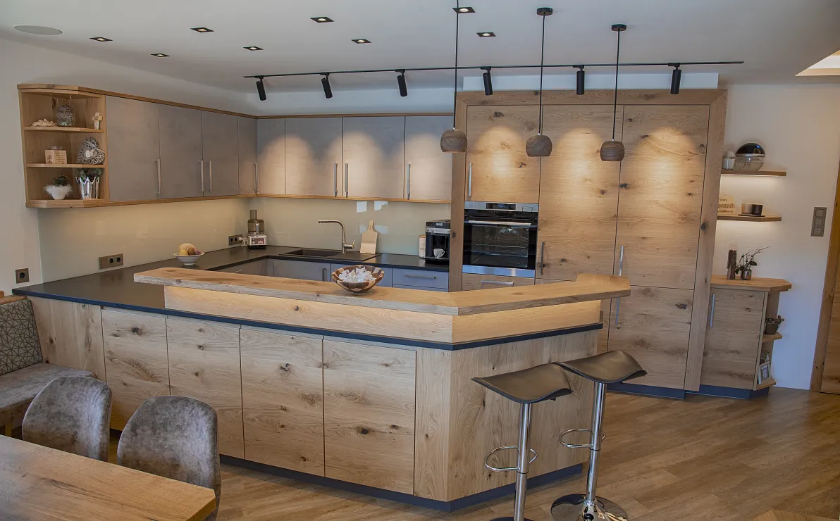 Moderne Küche mit Holzdekor, L-förmiger Arbeitsplatte, Barhockern und integrierten Elektrogeräten. Gemütliches und stilvolles Design mit offener Raumaufteilung.