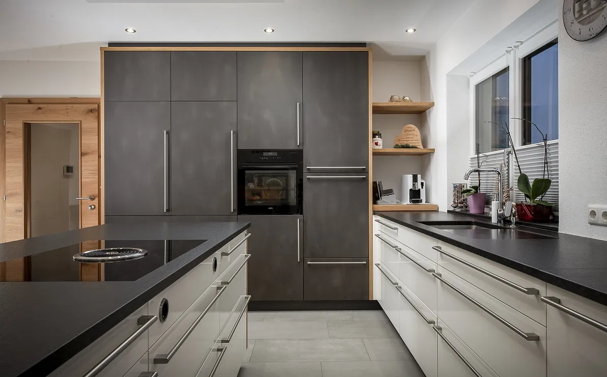 Moderne Küche mit dunklen Schränken, Herd und Spüle, minimalistisches Design. Heller Boden und Wandregale mit Dekorationen.