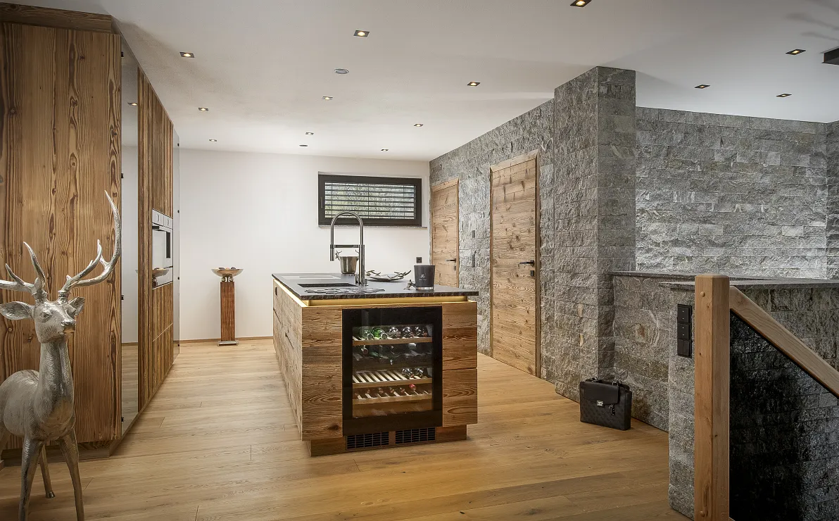 Moderne Küche mit Holzböden, Steinwänden und zentraler Insel. Ein Hirschmodell steht in der Ecke, natürliche und elegante Gestaltung.