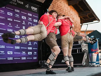 Drei Männer in traditioneller Kleidung führen einen dynamischen Tanz mit artistischen Sprüngen auf einer Bühne vor. Im Hintergrund ist ein Banner sichtbar.