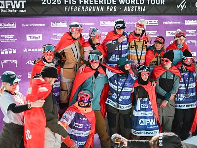 Gruppe von Freeridern mit roten Umhängen posiert vor einer Sponsorenwand bei der Freeride World Tour 2025 in Fieberbrunn, Österreich.