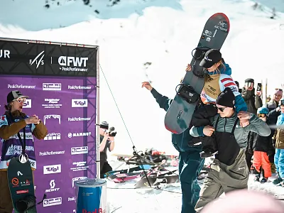 Menschen feiern bei einem Snowboard-Event in verschneiter Berglandschaft. Eine Person hebt ein Snowboard triumphierend in die Luft.