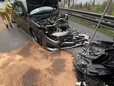 Ein Auto mit stark beschädigter Front steht auf einer Straße nach einem Unfall. Splitter und Streugut sind auf dem Asphalt verteilt. Einsatzkräfte sind vor Ort.