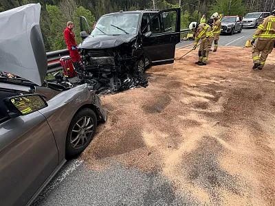 Zwei beschädigte Fahrzeuge nach einem Unfall, umgeben von Feuerwehrleuten in Einsatzkleidung auf einer Straße.