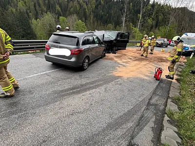 Ein Autounfall auf einer Landstraße, umgeben von Wald. Mehrere Feuerwehrleute sind vor Ort, um die Unfallstelle abzusichern.