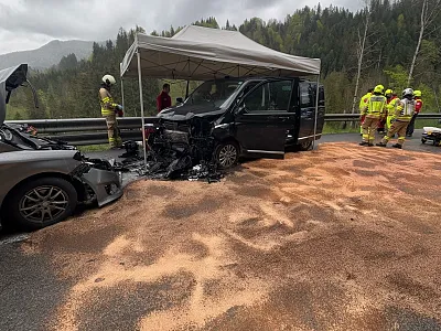 Verkehrsunfall auf einer Landstraße mit zwei beschädigten Fahrzeugen und mehreren Einsatzkräften vor Ort. Ein Zelt und verschüttetes Material sind sichtbar.