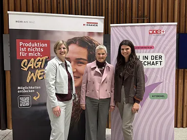 Drei Frauen stehen vor Plakaten bei einer Veranstaltung. Die Plakate thematisieren berufliche Möglichkeiten und Frauen in der Wirtschaft.