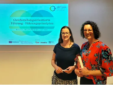 Zwei Frauen stehen vor einer Leinwand mit der Aufschrift "Gleichstellungsorientierte Führung - Führungsprinzipien" in einem Konferenzraum.