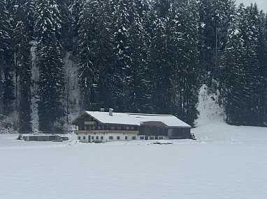 Eine verschneite Hütte steht am Rand eines zugefrorenen Sees, umgeben von dichten, schneebedeckten Tannen im Winter.