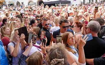 Eine große Menschenmenge bei einem Outdoor-Event, viele machen Fotos. Einige Personen in der Mitte scheinen besonders im Mittelpunkt zu stehen.