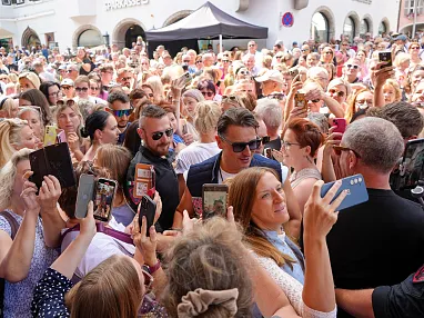 Eine große Menschenmenge bei einem Outdoor-Event, viele machen Fotos. Einige Personen in der Mitte scheinen besonders im Mittelpunkt zu stehen.