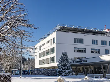 Ein modernes Gebäude bei klarem, blauem Himmel, umgeben von schneebedeckten Bäumen und Boden in einer winterlichen Landschaft.