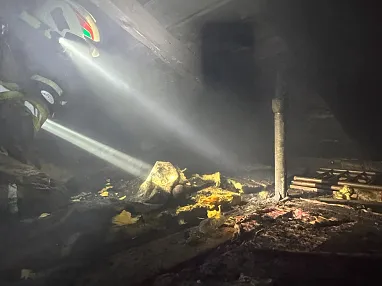 Ein Feuerwehrmann mit Helm und Schutzkleidung trägt eine Atemschutzmaske, während er unter Trümmern nach Überlebenden sucht. Taschenlampen strahlen durch den Rauch.