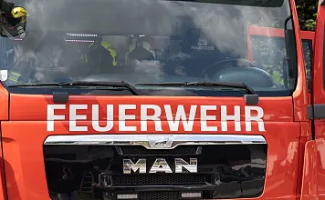 Rotes Feuerwehrauto der Marke MAN mit der Aufschrift "Hochfilzen" und "Feuerwehr" auf der Front. Teilweise verdeckte Fahrerkabine, im Freien abgestellt.