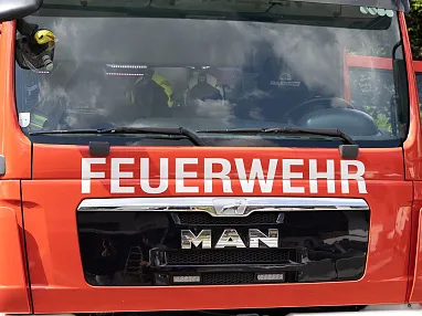 Rotes Feuerwehrauto der Marke MAN mit der Aufschrift "Hochfilzen" und "Feuerwehr" auf der Front. Teilweise verdeckte Fahrerkabine, im Freien abgestellt.