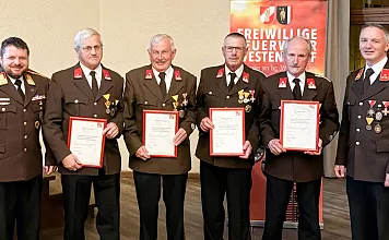 Eine Gruppe von Männern in Feuerwehruniformen hält Urkunden. Sie posieren vor einem Banner der Freiwilligen Feuerwehr für ein Gruppenfoto.