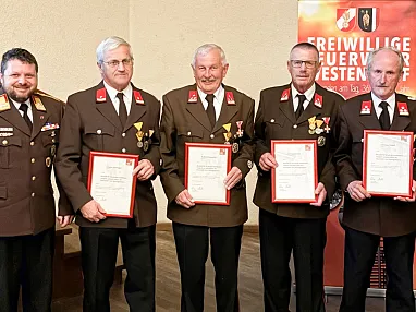 Eine Gruppe von Männern in Feuerwehruniformen hält Urkunden. Sie posieren vor einem Banner der Freiwilligen Feuerwehr für ein Gruppenfoto.