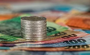 Ein Stapel Münzen steht auf mehreren übereinanderliegenden Euro-Banknoten in verschiedenen Farben und Werten. Das Bild symbolisiert Geld und Finanzen.