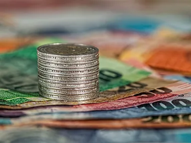 Ein Stapel Münzen steht auf mehreren übereinanderliegenden Euro-Banknoten in verschiedenen Farben und Werten. Das Bild symbolisiert Geld und Finanzen.