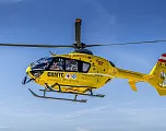 Gelber Rettungshubschrauber des ÖAMTC fliegt am klaren Himmel. Er trägt medizinische Symbole und ist in Österreich registriert.