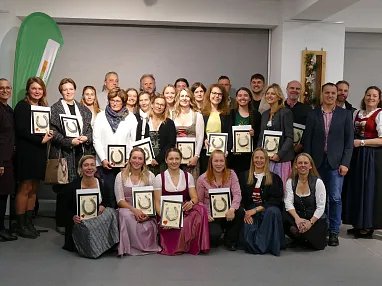 Gruppe von Menschen posiert lächelnd in traditioneller Kleidung und hält gerahmte Auszeichnungen auf einer festlichen Veranstaltung.