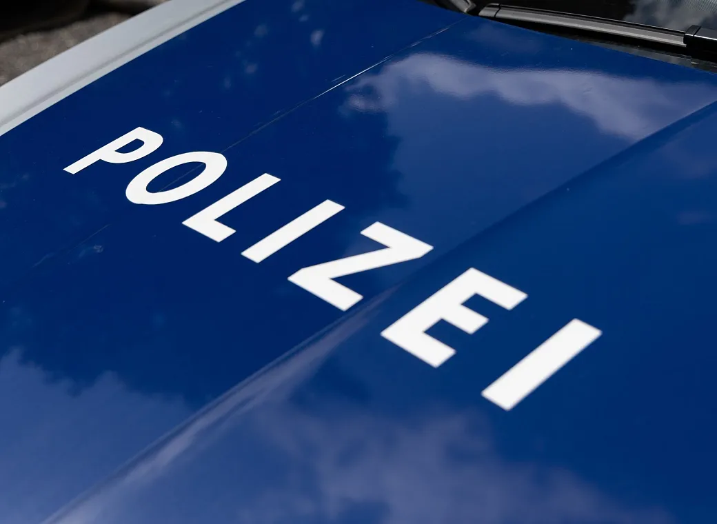 Nahaufnahme einer blauen Motorhaube eines Polizeiwagens mit dem weißen Schriftzug "POLIZEI". Das Licht reflektiert auf der glatten Oberfläche.