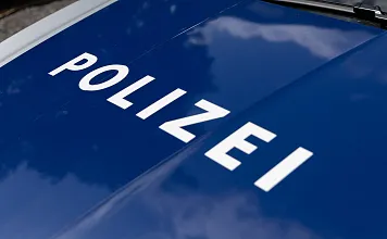 Nahaufnahme einer blauen Motorhaube eines Polizeiwagens mit dem weißen Schriftzug "POLIZEI". Das Licht reflektiert auf der glatten Oberfläche.
